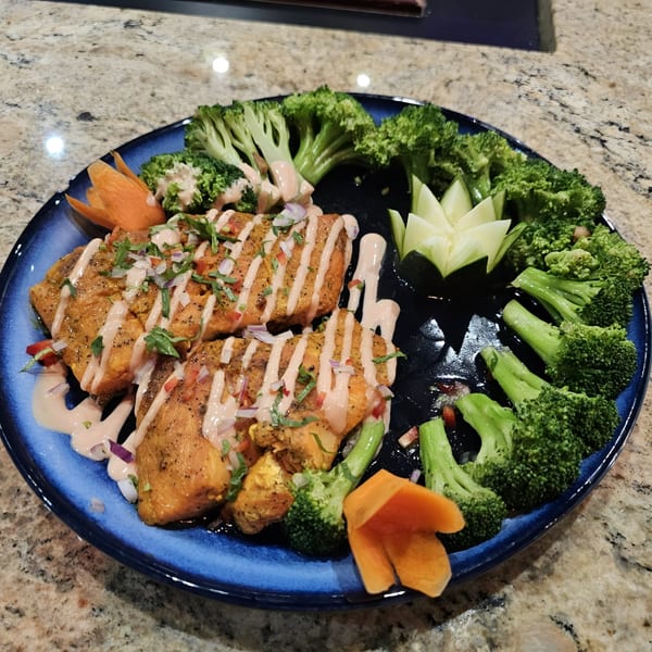 Indian paneer tikka with broccoli, garnished with sauce, herbs, and carved vegetables on a blue plate.