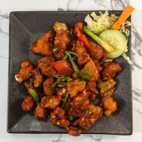 Indian chili chicken with bell peppers and green onions, garnished with cucumber and carrots.