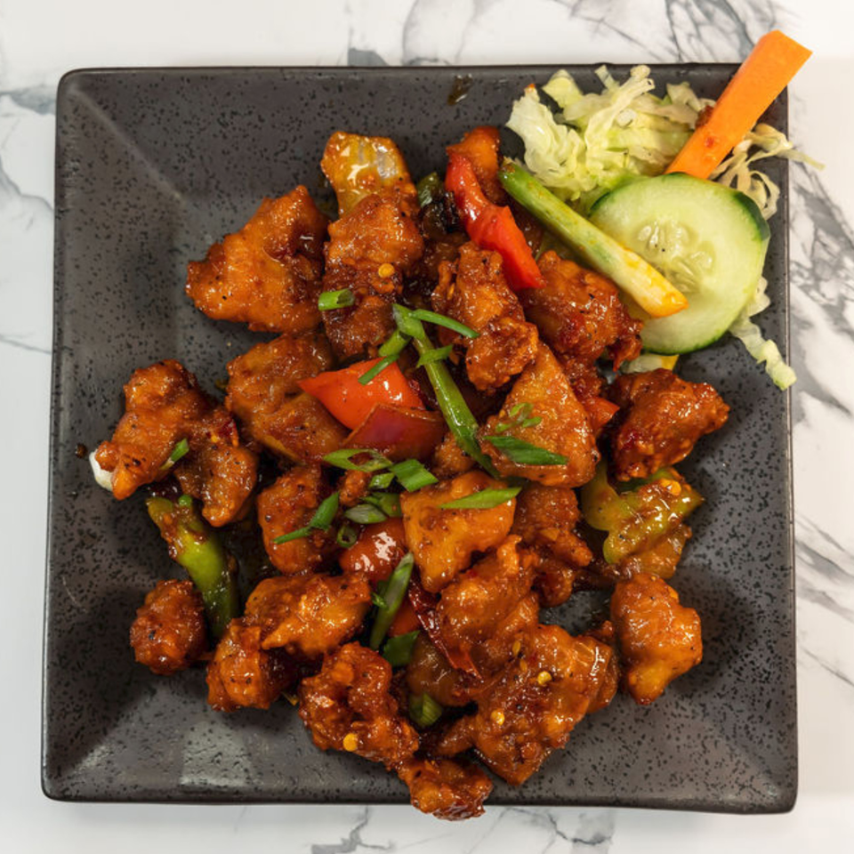 Indian chili chicken with bell peppers and green onions, garnished with cucumber and carrots.