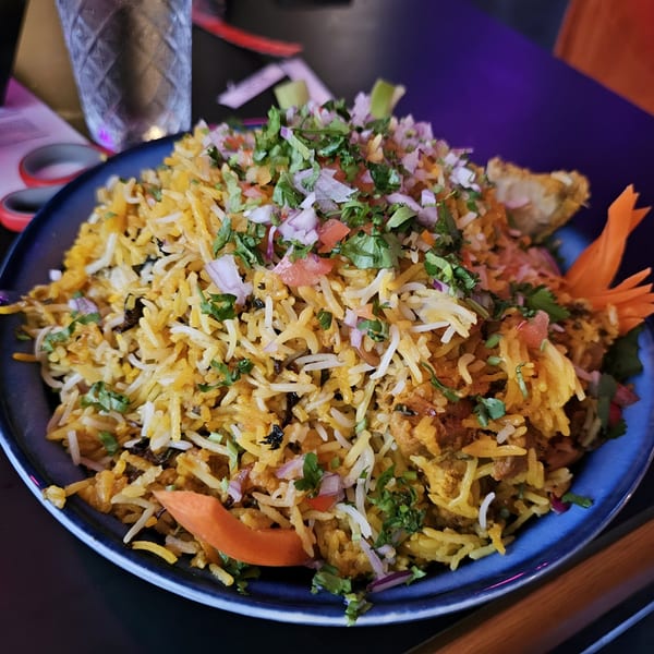 A large serving of Indian biryani, topped with chopped cilantro, red onions, and tomatoes.