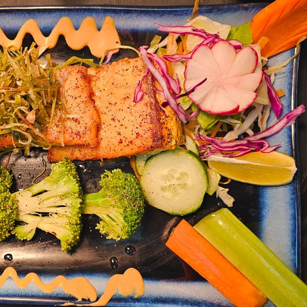 Grilled salmon with broccoli, cucumber, radish, and a side salad on a blue plate.