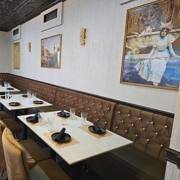 Elegant dining room at The Opulent Restaurant with brown tufted booths, white tables, and framed artwork.