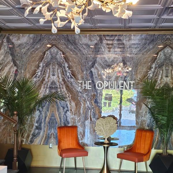 The Opulent Restaurant and Lounge's entrance with marble walls, orange chairs, and a decorative chandelier.