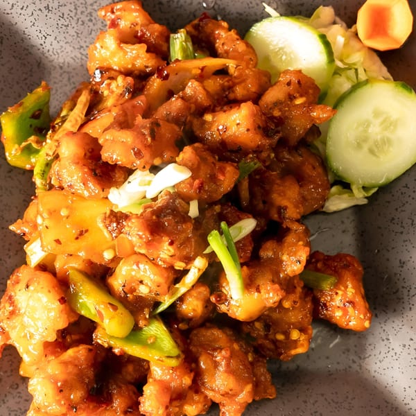 Close-up of Indian chili chicken with bell peppers, onions, and a side of cucumber slices.