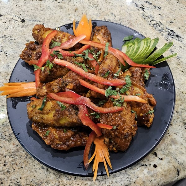 Indian chicken wings, garnished with red bell peppers, cilantro, and carved carrots on a black plate.