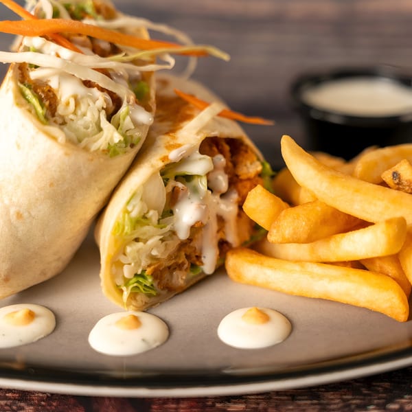 Two Indian chicken wraps with lettuce, cabbage, and sauce, served with golden french fries.