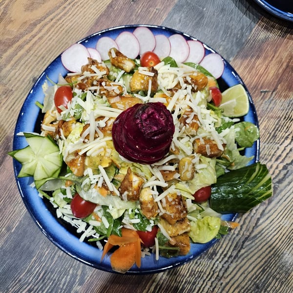 A vibrant Indian salad with chicken, cheese, cherry tomatoes, and a beet rose on a blue plate.