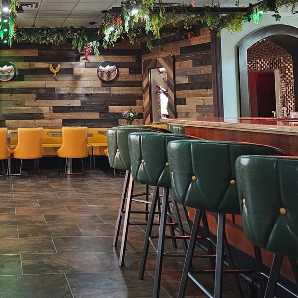 The Opulent Restaurant and Lounge interior with bar stools, yellow booths, and a wooden accent wall.