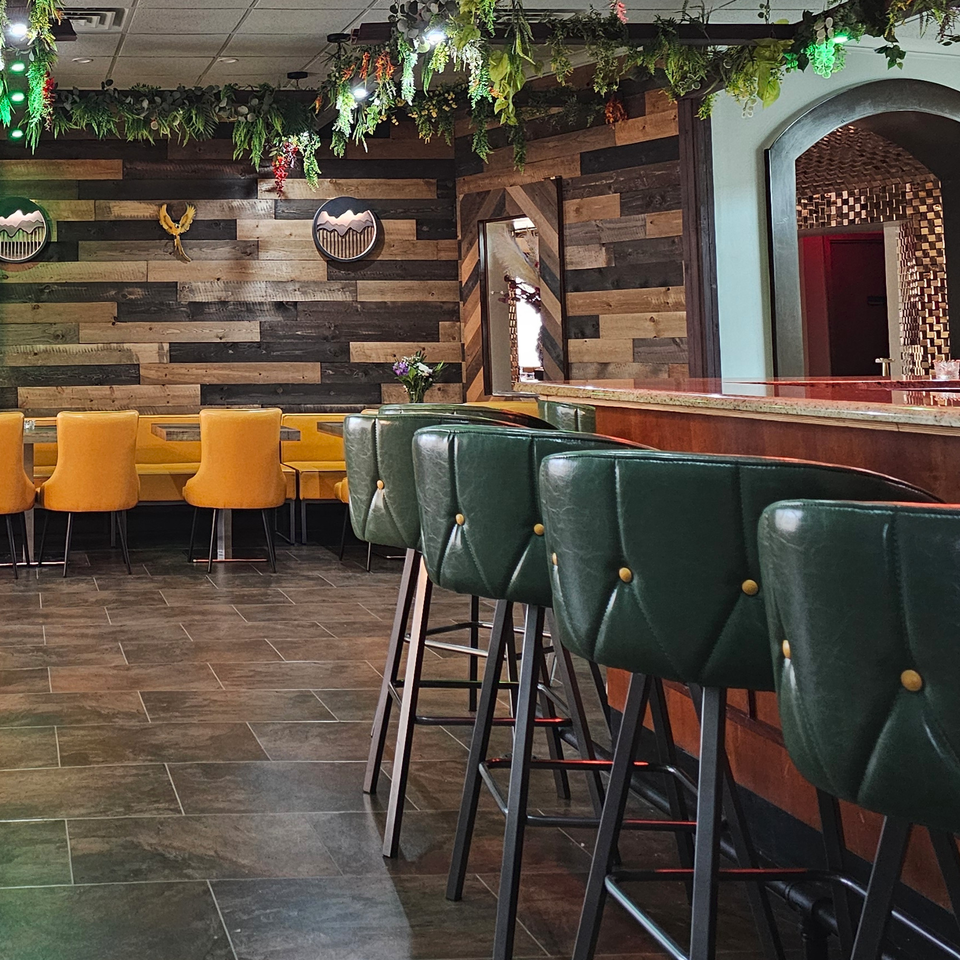 The Opulent Restaurant and Lounge interior with bar stools, yellow booths, and a wooden accent wall.