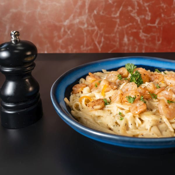 Creamy shrimp pasta with parsley and black pepper in a blue bowl next to a pepper grinder.