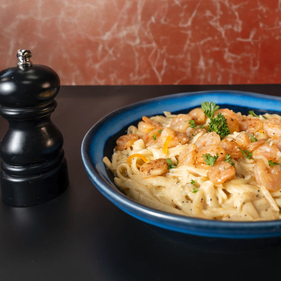 Creamy shrimp pasta with parsley and black pepper in a blue bowl next to a pepper grinder.