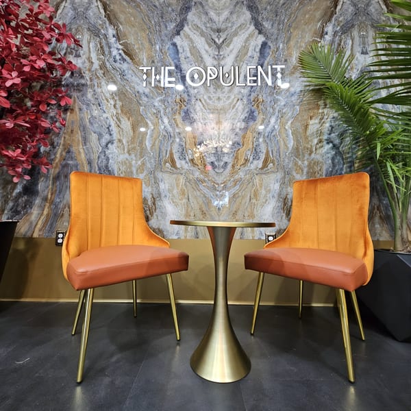 The Opulent Restaurant and Lounge's entrance features a marble wall, two orange chairs, and a gold table.