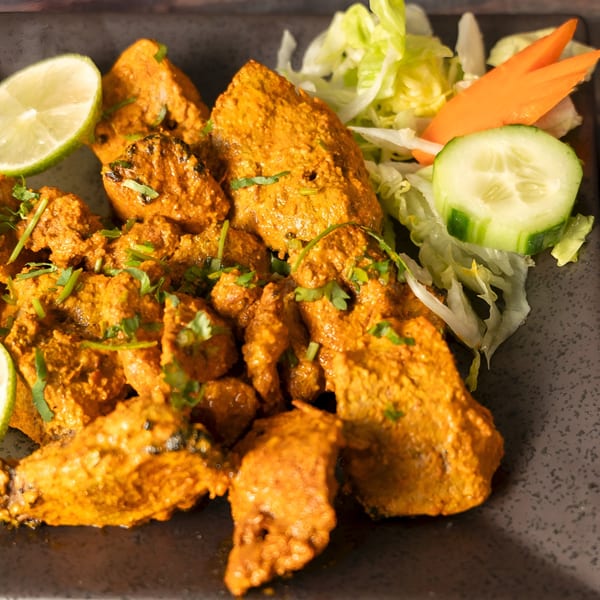 Indian chicken tikka with cilantro, lime, and a side salad on a dark plate.