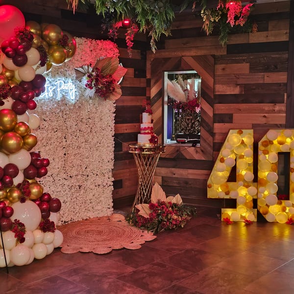 A festive party setup with balloons, a cake, and illuminated "40" numbers against a wooden wall.