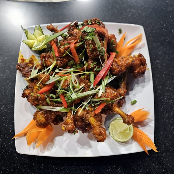 Indian chicken lollipops garnished with mint, peppers, scallions, carved cucumber, carrot, and lime.