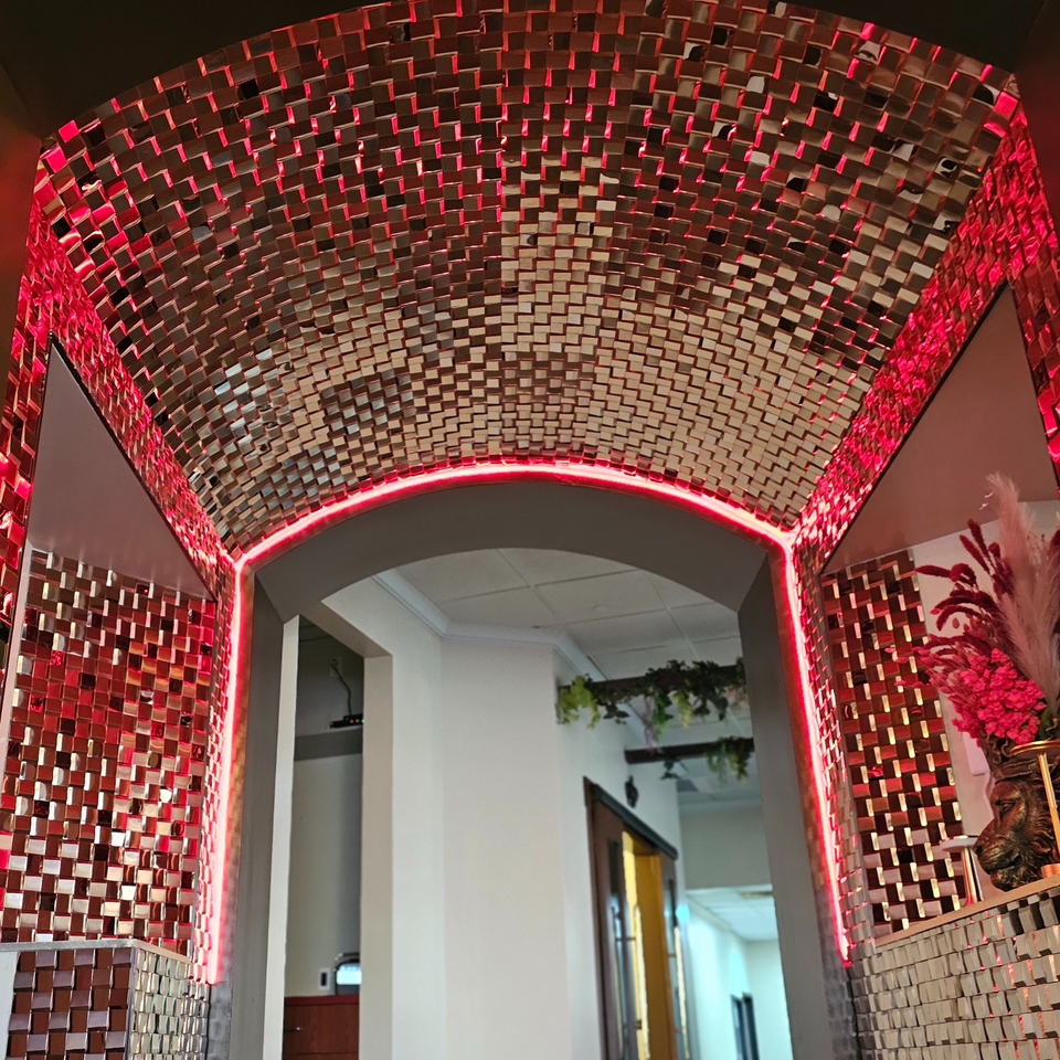 A hallway with a mirrored, arched ceiling and walls, illuminated by red neon lights.