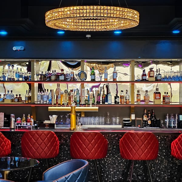 The Opulent Restaurant and Lounge's bar with red stools, liquor bottles, and a crystal chandelier.
