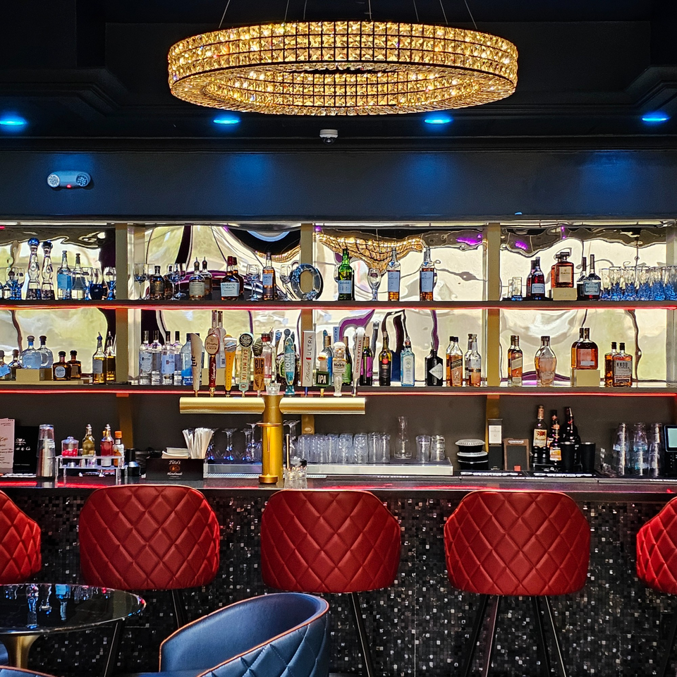The Opulent Restaurant and Lounge's bar with red stools, liquor bottles, and a crystal chandelier.
