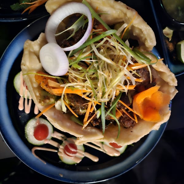 Indian flatbread wrap filled with meat, shredded vegetables, onions, and sauce, on a blue plate.