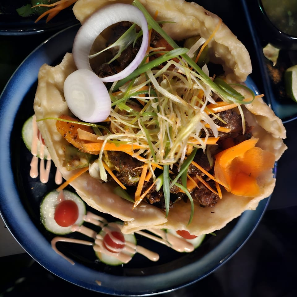 Indian flatbread wrap filled with meat, shredded vegetables, onions, and sauce, on a blue plate.