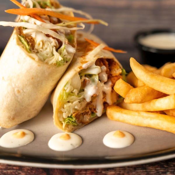 Two Indian chicken wraps with lettuce, shredded carrots, and white sauce, served with fries.