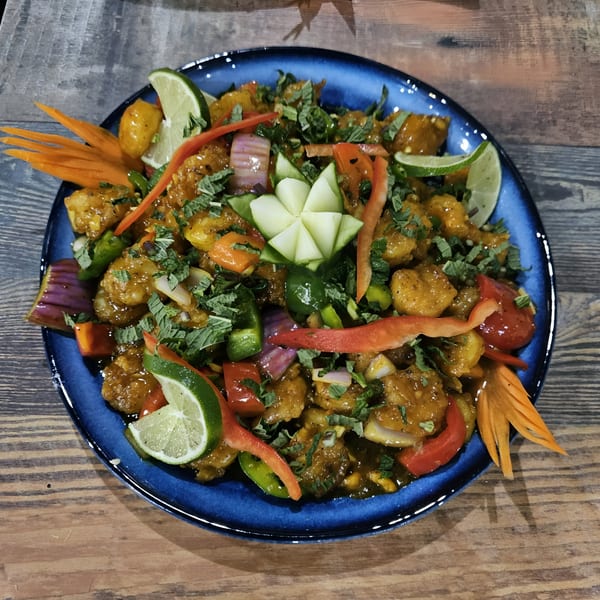 Indian chili chicken, garnished with lime, peppers, and herbs, served on a blue plate.