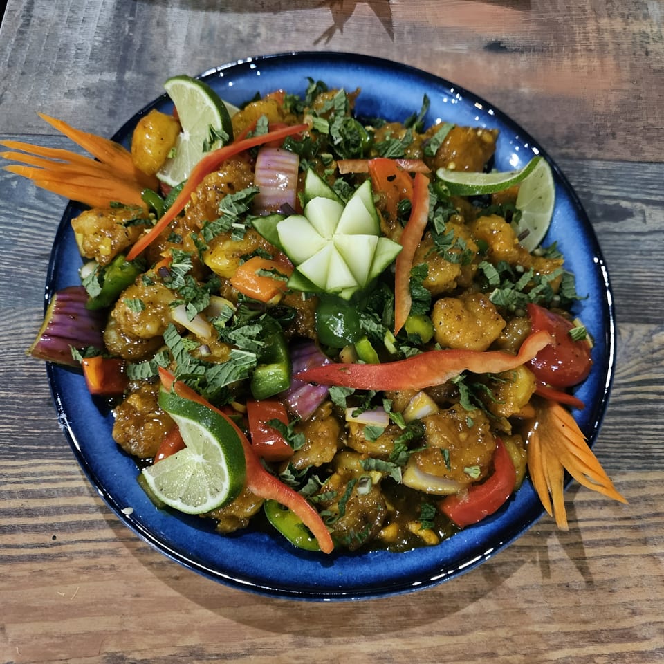 Indian chili chicken, garnished with lime, peppers, and herbs, served on a blue plate.