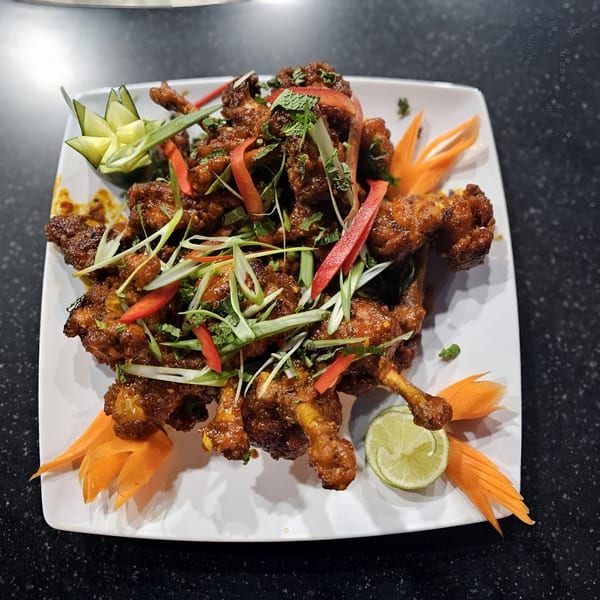 Indian chicken lollipops garnished with herbs, peppers, and carved vegetables on a white plate.