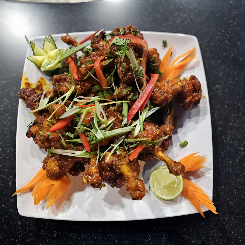 Indian chicken lollipops garnished with herbs, peppers, and carved vegetables on a white plate.