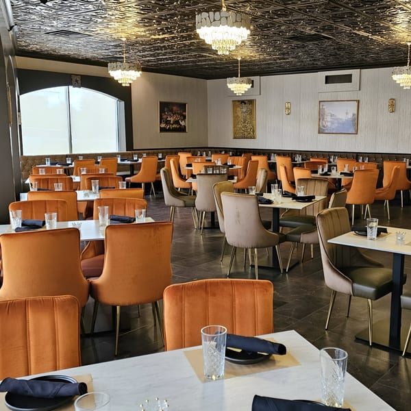 The Opulent Restaurant and Lounge's dining room with orange and beige chairs, set tables, and chandeliers.