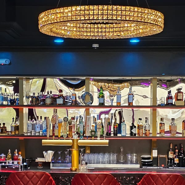 A luxurious bar at The Opulent Restaurant and Lounge, featuring a crystal chandelier and liquor bottles.