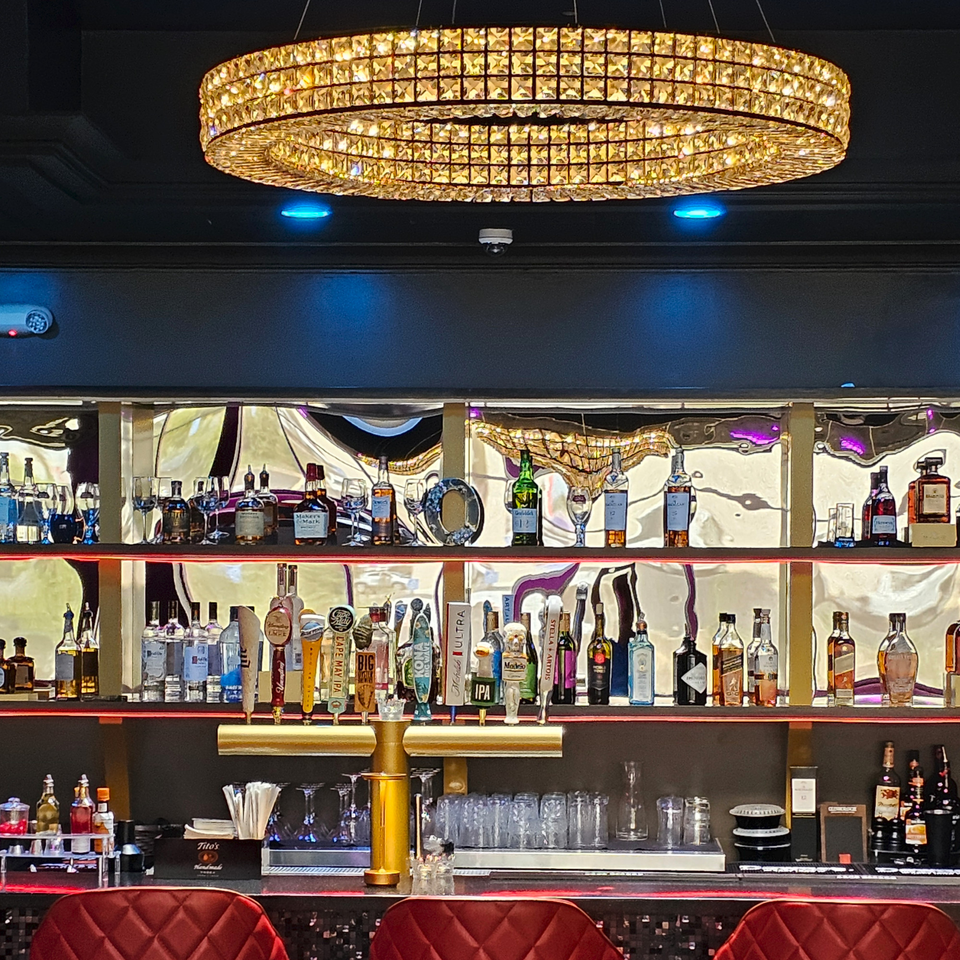 A luxurious bar at The Opulent Restaurant and Lounge, featuring a crystal chandelier and liquor bottles.