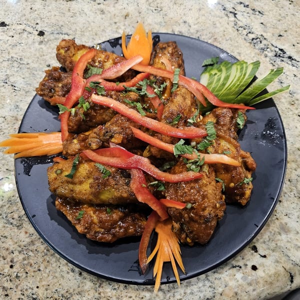 Indian chicken wings with red peppers, mint, and carved vegetables on a black plate.