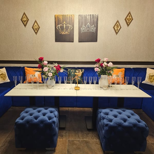 A private dining area with blue velvet seating, a white table set with champagne flutes, and floral arrangements.
