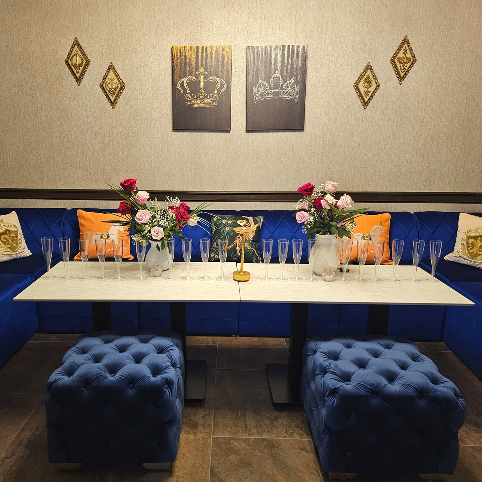 A private dining area with blue velvet seating, a white table set with champagne flutes, and floral arrangements.