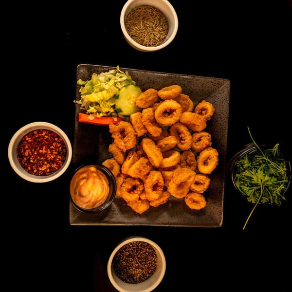 Crispy fried calamari rings with a side of salad, dipping sauce, and various spices.