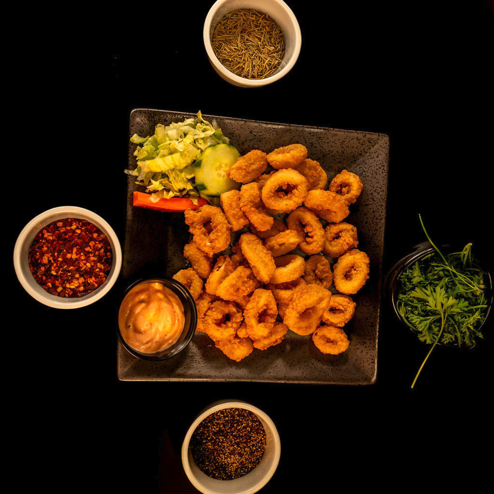 Crispy fried calamari rings with a side of salad, dipping sauce, and various spices.