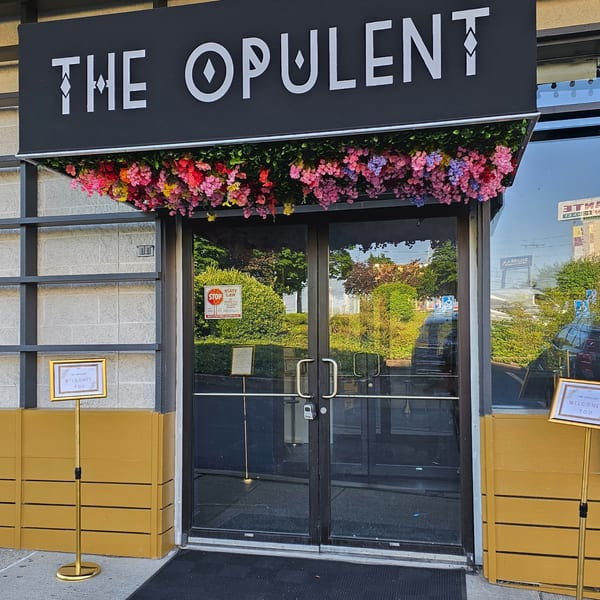 The Opulent Restaurant and Lounge entrance with a black sign, colorful flowers, and glass doors.