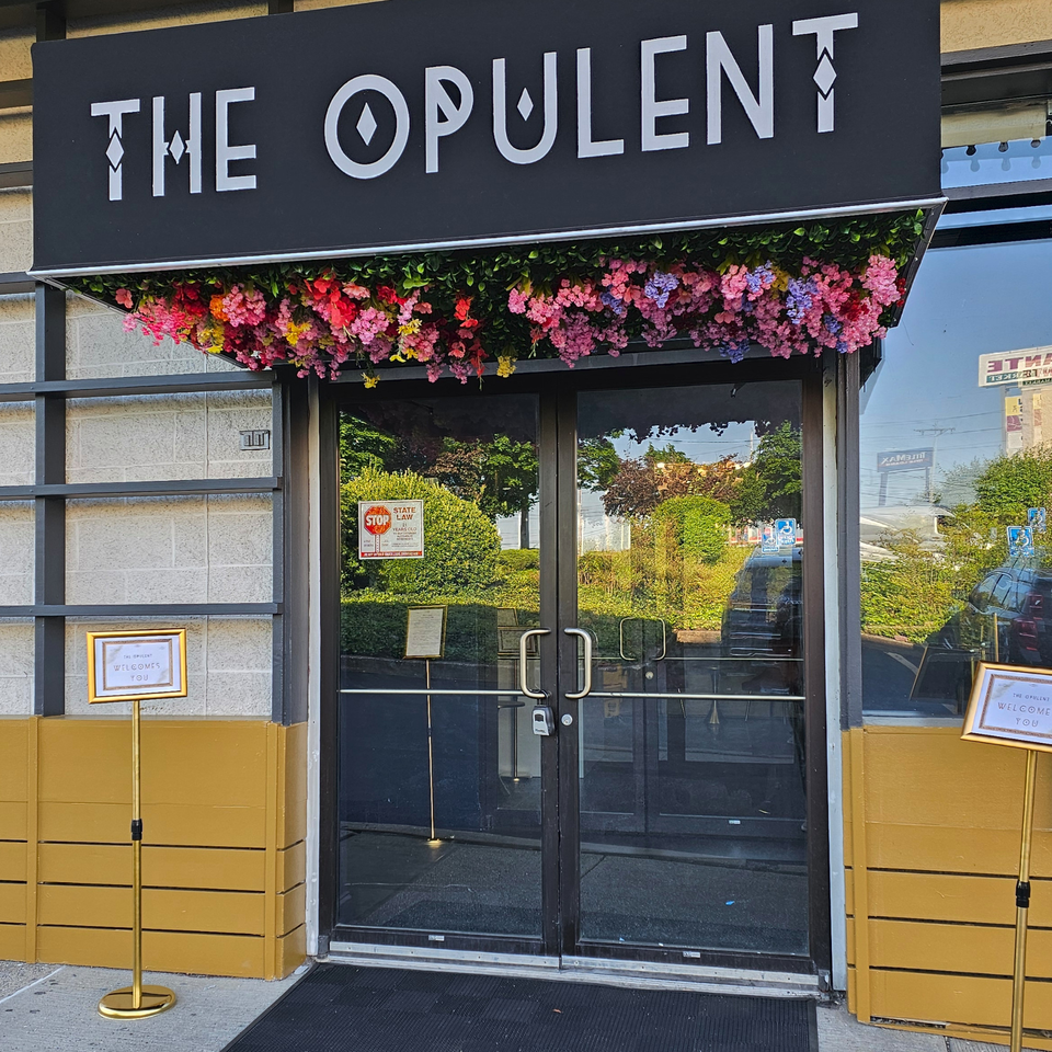 The Opulent Restaurant and Lounge entrance with a black sign, colorful flowers, and glass doors.